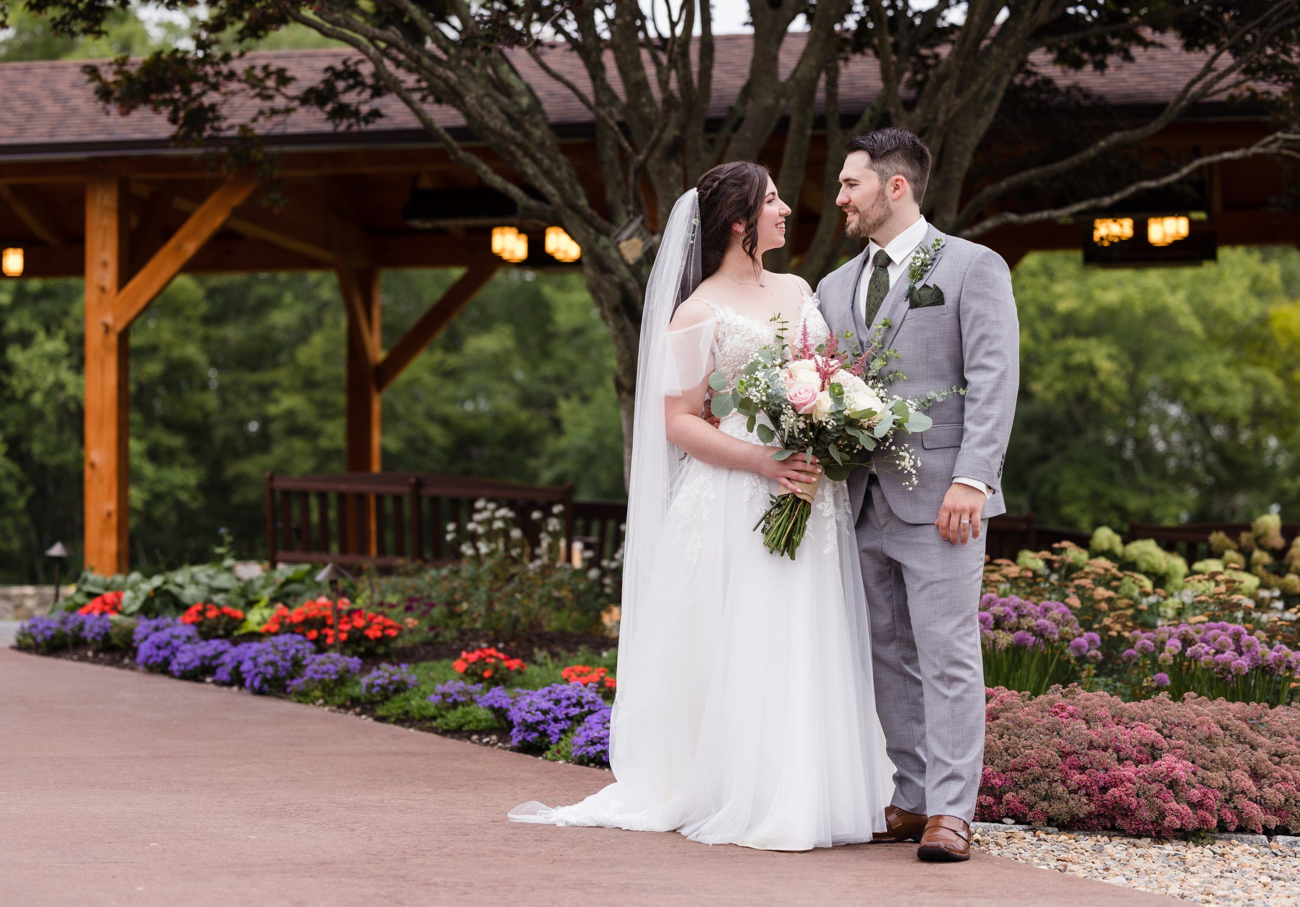 Bride and groom stand posed in front of garden.